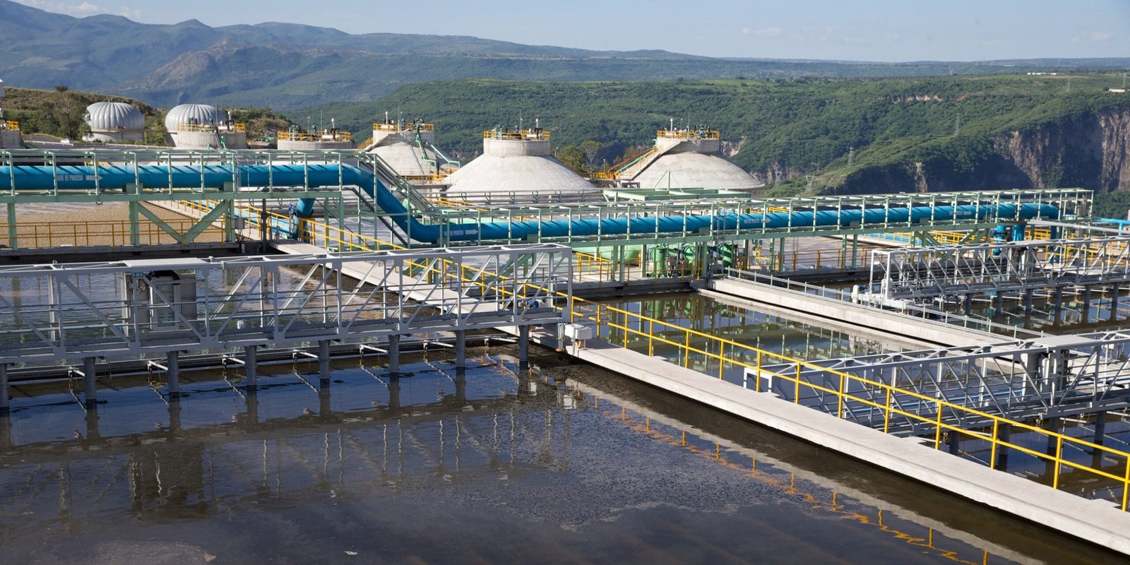 "Instalaciones industriales de tratamiento de agua con tuberías y tanques en un entorno montañoso.