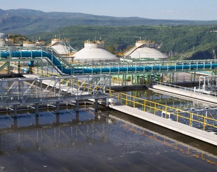 "Instalaciones industriales de tratamiento de agua con tuberías y tanques en un entorno montañoso.